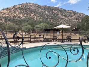 A swimming pool with a metal fence and spiral design, surrounded by outdoor furniture and a mountain backdrop.