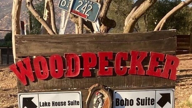 Un panneau en bois indiquant « WOODPECKER HOLLOW » et des flèches directionnelles menant à « Lake House Suite » et « Boho Suite ».