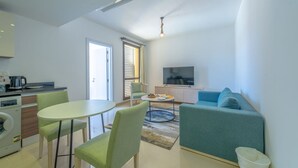 A modern living room with a sofa, a TV, and a dining area with chairs and a table. - Vesta - Luxury APT - 1BR - Gcribs I (El Gouna)