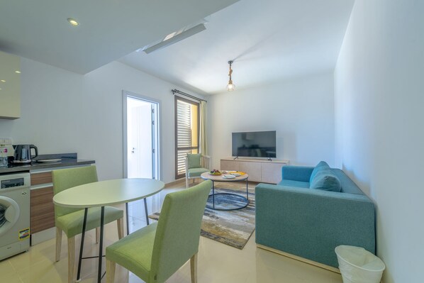 A modern living room with a sofa, a TV, and a dining area with chairs and a table. - Vesta - Luxury APT - 1BR - Gcribs I (El Gouna)