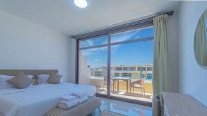 A hotel room with a large bed, a small desk, a balcony with a table and chairs, and a view of buildings. - Vesta - Luxury APT - 1BR - Gcribs I (El Gouna)