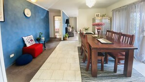 A dining area with a wooden table and chairs, a red sofa, and a blue wall with a clock. - Entire Home In Werribee On the Best Possible Location. (Werribee)