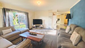 A living room with a sofa, a coffee table, a flat-screen TV, and a large window with curtains. - Entire Home In Werribee On the Best Possible Location. (Werribee)