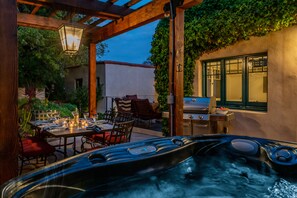 A hot tub under a wooden pergola with a table and chairs nearby, surrounded by greenery and a view of a building. - Historic Adobe Retreat | Firepit Courtyard, Private Hot Tub & Timeless Character (Santa Barbara)