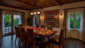Comedor con mesa de madera dispuesta para seis personas, rodeada de sillas, con vistas a la vegetación a través de amplios ventanales.