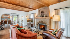 Amplia sala de estar con chimenea, sofás de cuero y un comedor con vistas al exterior.