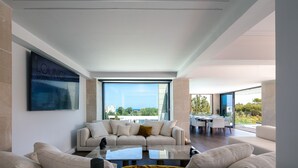 A modern living room with a large sectional sofa, a coffee table, and a dining area with a table and chairs. - 250m2 pool, Daily Housekeeping, Spa, 300m to beach and Shops: by etouri (Chania)