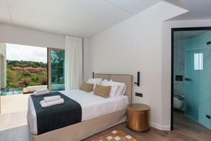 A modern bedroom with a large bed, a glass shower enclosure, and a view of a natural landscape. - 250m2 pool, Daily Housekeeping, Spa, 300m to beach and Shops: by etouri (Chania)