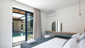 A modern hotel room with a bed, a large mirror, a ceiling light, and a view of an outdoor swimming pool. - Ikritis Villa Ι - 1,2Km to beach & sea views! (Chania)