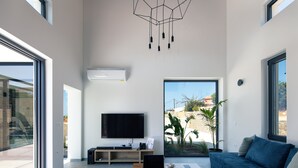 A modern living room with a large flat-screen TV, a laptop, a coffee cup, and a blue sofa. - Ikritis Villa Ι - 1,2Km to beach & sea views! (Chania)