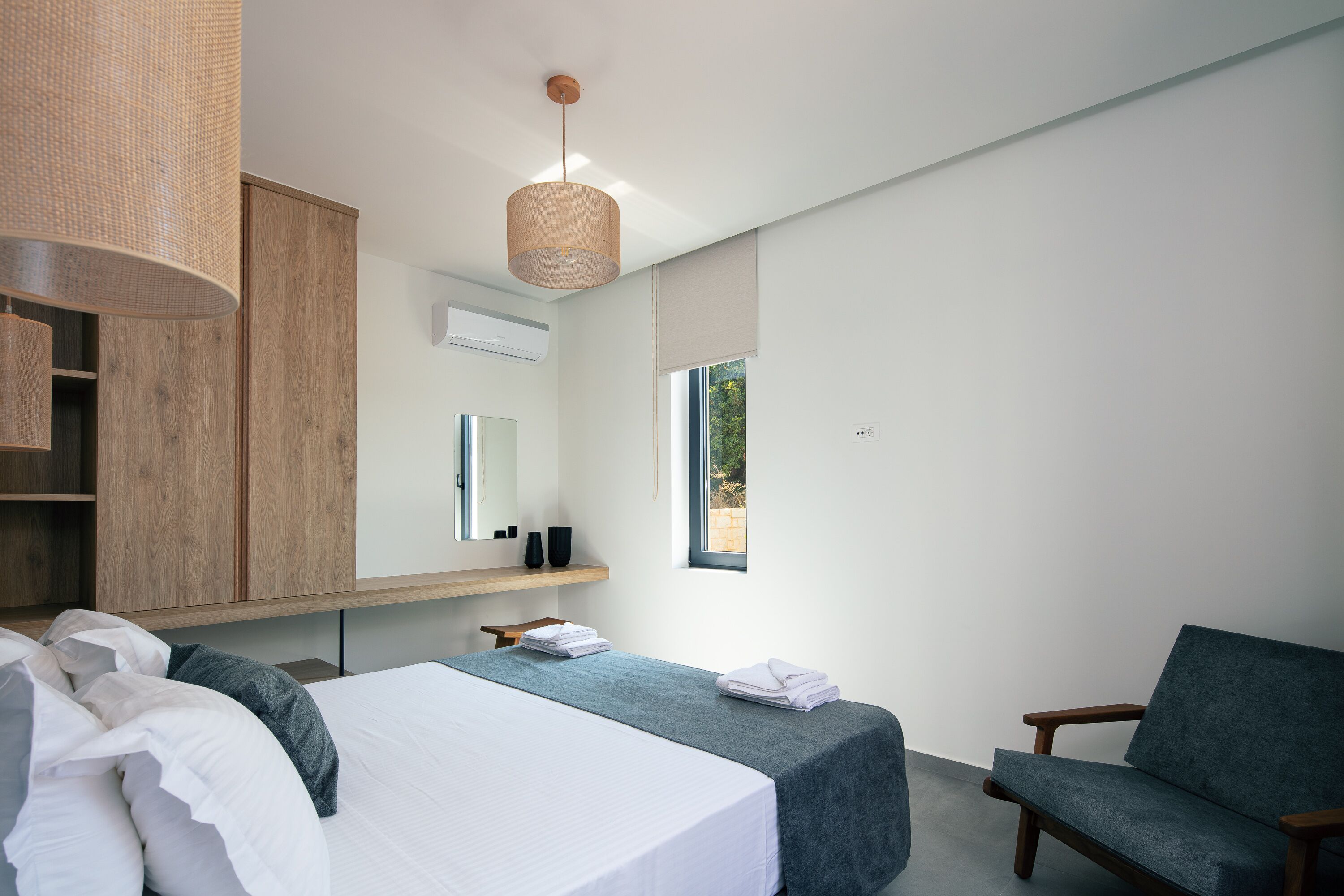 A modern bedroom with a bed, a chair, a bedside table, a hanging light, and a window.