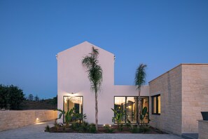Ein modernes Gebäude mit Flachdach, großen Fenstern und einem gepflegten Garten mit Palmen und anderer Bepflanzung.