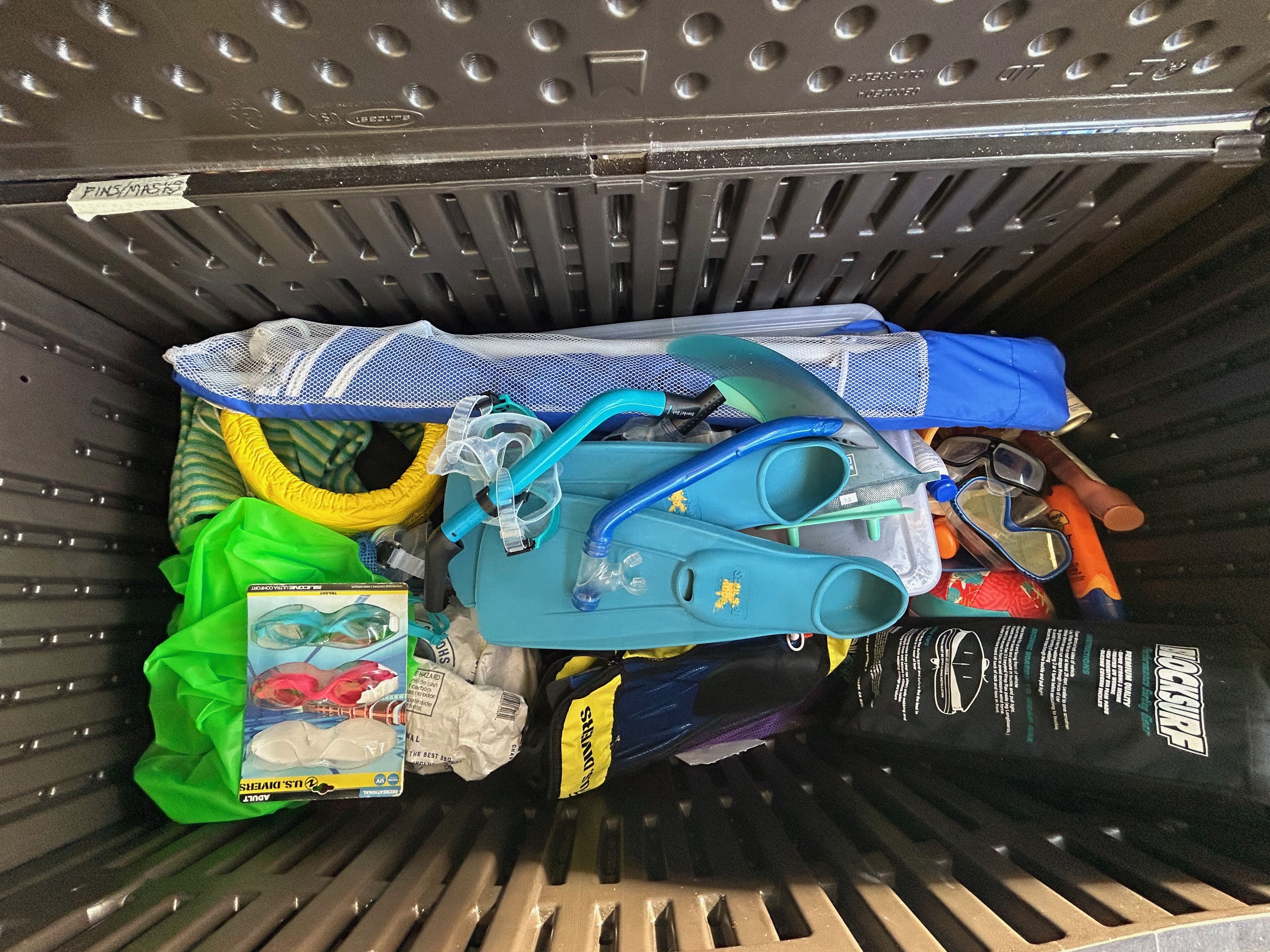 Un bac de rangement rempli de divers objets, notamment un tuba, une paire de lunettes de plongée et un sac noir étiqueté « LOCKGURF ».