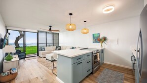 A modern kitchen with a central island, a dining area with a view, and a living space with a sofa and a lamp.
