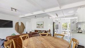 A spacious living area with a large wooden dining table surrounded by wooden chairs, a leather sofa, and a hanging wall decoration. - Rye Beach Abode - STAY 3 PAY 2 SPECIAL OFFER! Expires 1st September 2025 (Rye)