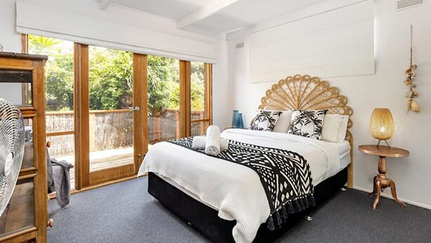A bedroom with a bed, a wooden headboard, a bedside table, and a view of the outdoors through a sliding door. - Rye Beach Abode - STAY 3 PAY 2 SPECIAL OFFER! Expires 1st September 2025 (Rye)