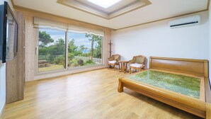 A spacious room with a large sliding glass door leading to a garden, a wooden bed, two chairs, and a small table.