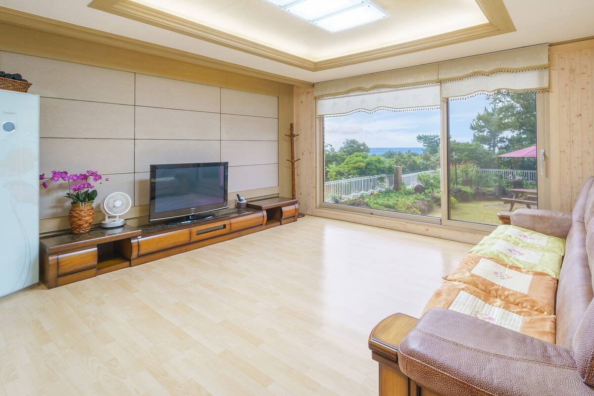 Un salón espacioso con televisor grande, muebles de madera y vistas al exterior.