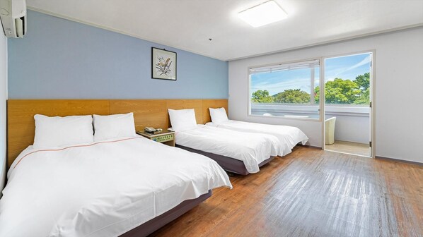 A hotel room with two beds, a wooden headboard, a framed picture on the wall, and a large window offering a view of trees. - Jeju Honeycrown Hotel (Jeju City)