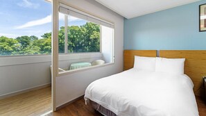 A bedroom with a large bed, a window with a view of trees, and a small table with chairs. - Jeju Honeycrown Hotel (Jeju City)