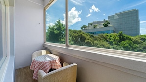 Un balcon avec une chaise en osier et une petite table recouverte d’une nappe à carreaux.