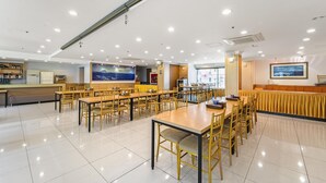 Un vaste espace dédié à la restauration, avec de nombreuses tables et chaises, un comptoir d’accueil et une grande fenêtre offrant une vue sur le paysage urbain.