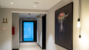 Un couloir orné d’un grand tableau encadré, muni d’un détecteur d’incendie et de panneaux indiquant les sorties de secours.