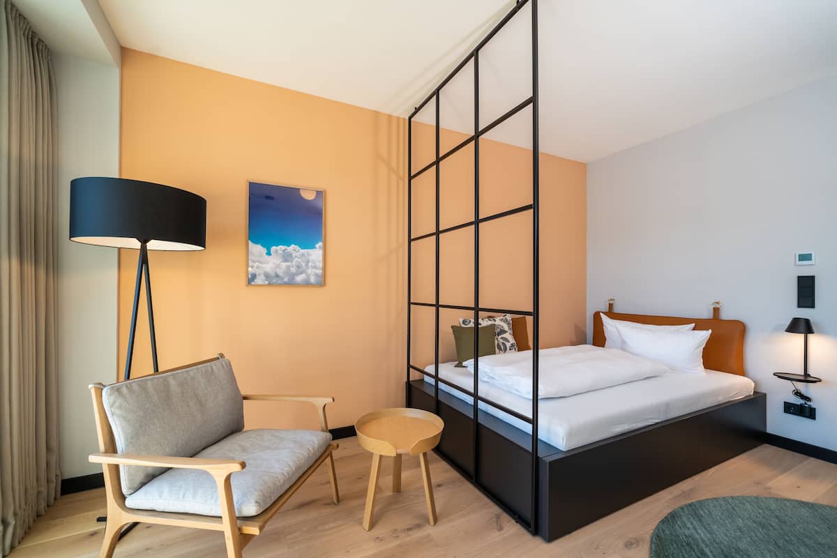 Ein Hotelzimmer mit Bett, Stuhl, kleinem Tisch, Stehlampe und einem Bild an der Wand.