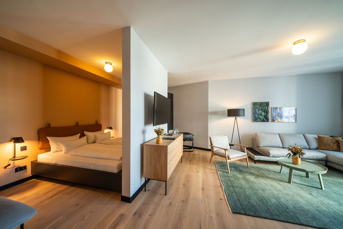 Ein modernes Hotelzimmer mit Bett, Nachttisch, Lampe und einer Sitzecke mit Couchtisch.