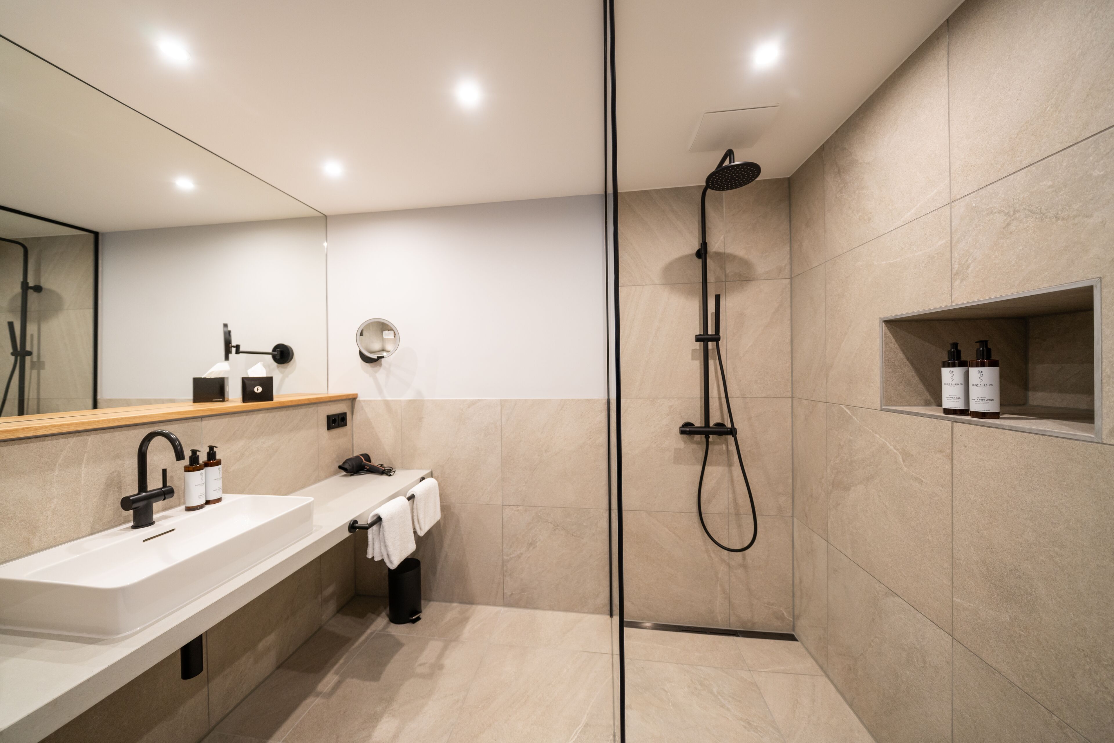 Un baño moderno con un espejo grande, un lavabo, una ducha y un estante con artículos de aseo.