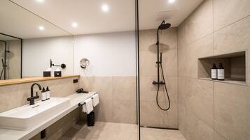 Un baño moderno con un espejo grande, un lavabo, una ducha y un estante con artículos de aseo.