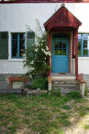 Una casa con puerta azul, contraventanas verdes y chimenea de ladrillo.