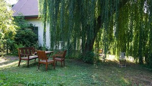 An outdoor seating area with a table and chairs, surrounded by lush greenery and a weeping willow tree. - Romantisches Ferienhaus Mitten in der Natur (Wiesbaden)