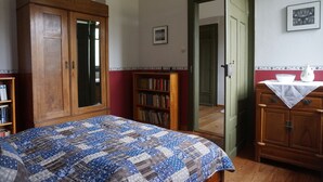 A bedroom with a large wooden wardrobe, a bookshelf, a quilted bedspread, and a small table with a vase. - Romantisches Ferienhaus Mitten in der Natur (Wiesbaden)