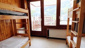Une chambre avec un lit superposé en bois, une grande fenêtre et un radiateur.