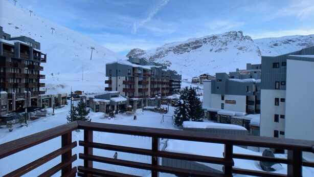 Une ville de montagne enneigée, avec des bâtiments modernes, dont un hôtel doté de balcons, et un télésiège visible au loin.