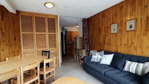 Une pièce chaleureuse avec un mur en bois, un canapé bleu, une table à manger en bois avec des chaises et une petite table ronde.