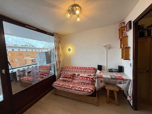 Une chambre avec une grande fenêtre, un lit recouvert d’une literie à motifs, une table de chevet, une lampe et une étagère avec divers objets.