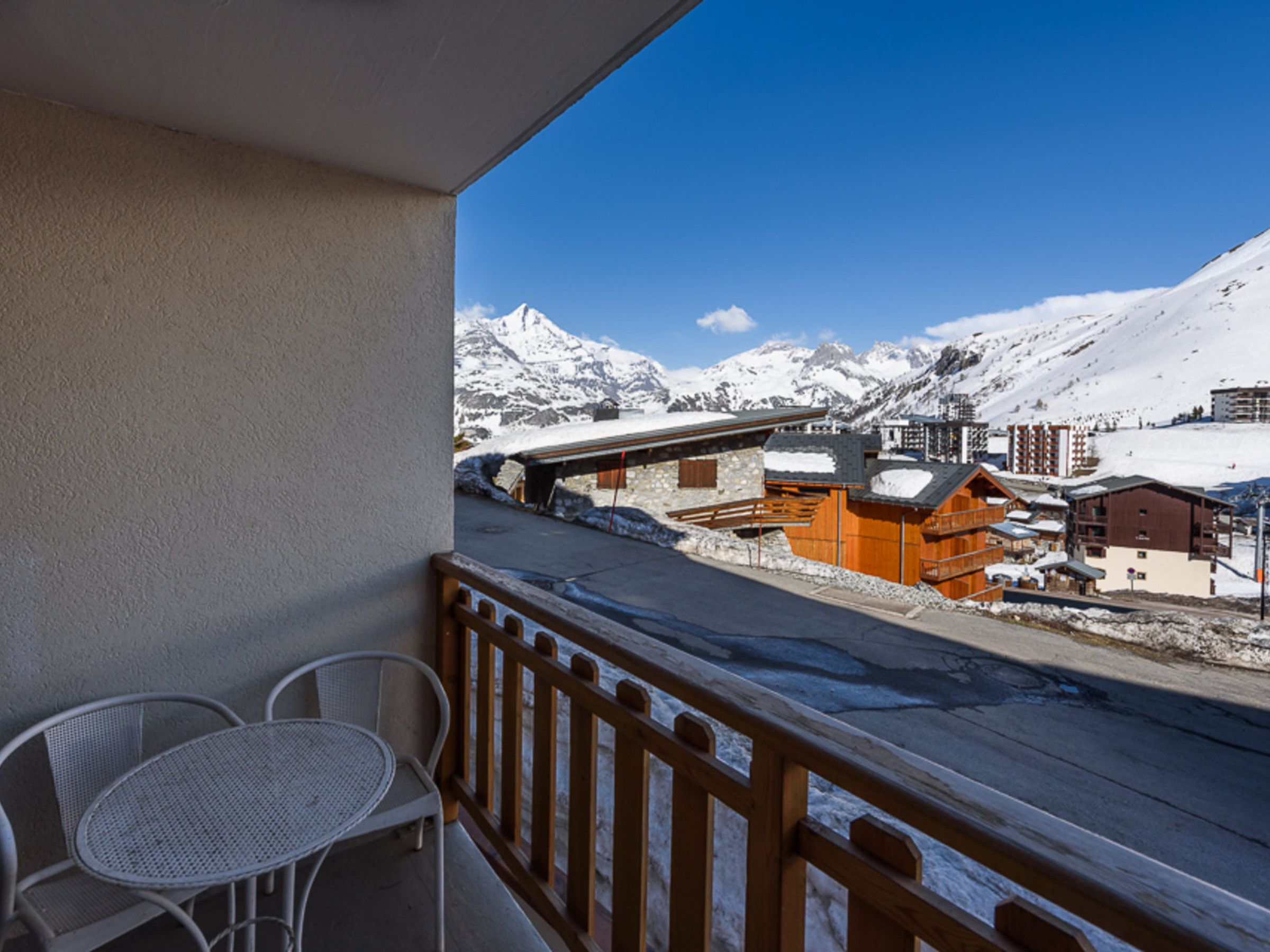 Un balcon offrant une vue sur un paysage montagneux enneigé, une clôture en bois et une table avec des chaises.