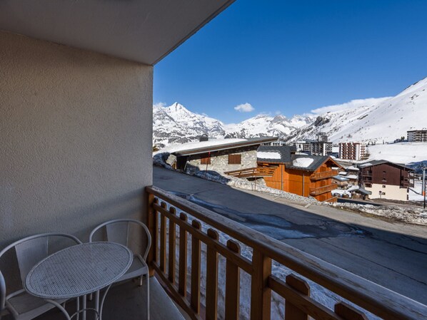 A balcony with a view of a snowy mountain landscape, a wooden fence, and a table with chairs.