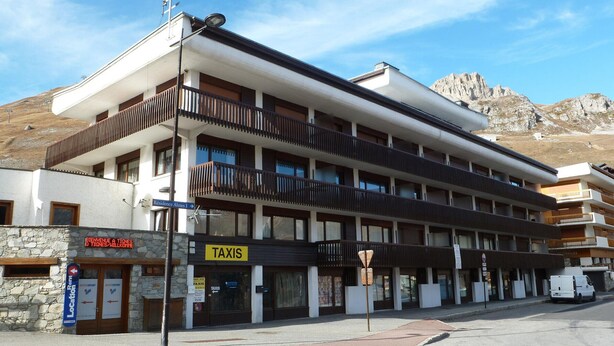 A multi-story building with a 'TAXIS' sign, a stone facade, and a mountain backdrop.