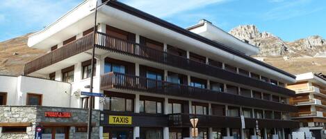 Un edificio de varios pisos con entrada en la planta baja señalizada con 'TAXIS' y un letrero que indica servicios 'INTERSPORT'.