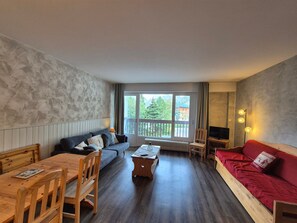A living room with a sofa, a red couch, a wooden table, and a television.