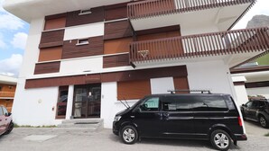 A modern building with a flat roof, multiple balconies, and a black van parked in front.