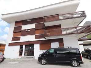 A modern building with a flat roof, multiple balconies, and a black van parked in front.