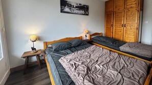 A bedroom with two beds, a wooden wardrobe, a small bedside table with a lamp, and a framed picture on the wall.