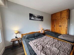 A bedroom with two beds, a wooden wardrobe, a small bedside table with a lamp, and a framed picture on the wall.