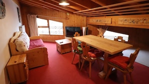 A cozy cabin interior with a wooden dining table, chairs, a sofa, and a television. - Comfortable Apartment in the Heart of Tignes le Lac, Ideal for 6 People (Tignes)