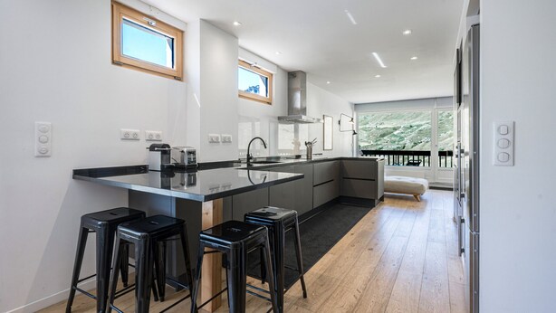 A modern kitchen with a central island, bar stools, and a view to a balcony.
