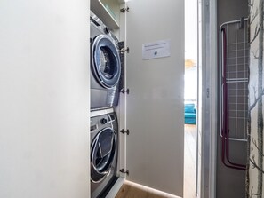 A laundry room with two stacked front-loading washing machines, a drying rack, and a sign on the door.
